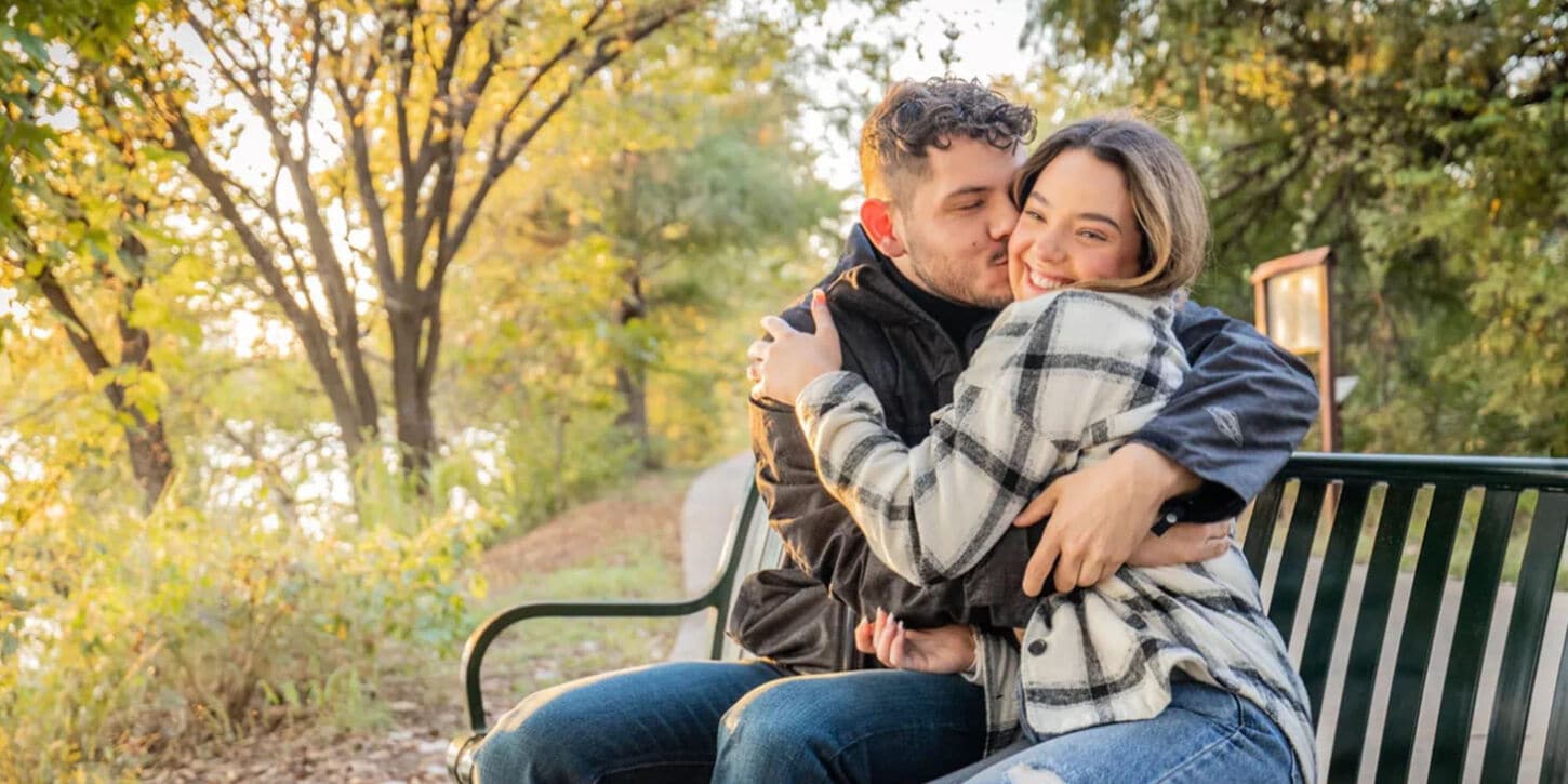 Ashley and Jonathon sitting on a bench in a park hugging for a picture